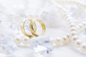 Two golden rings with pearl necklace and on white background