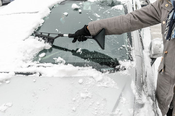 Woman cleaning car from the snow with brush. People in snowy cold weather in winter and...