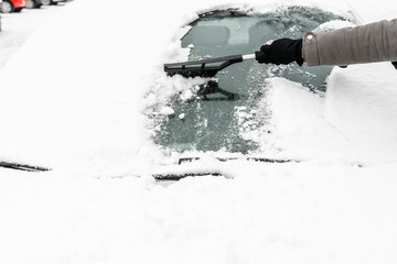 Woman cleaning car from the snow with brush. People in snowy cold weather in winter and...