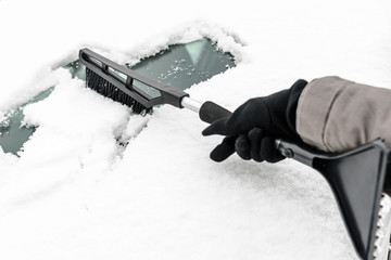 Woman cleaning car from the snow with brush. People in snowy cold weather in winter and...