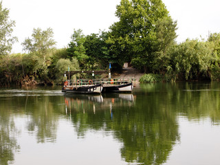 A river ferry consisting of two boats and a deck floats across a calm river.