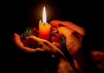 Burning Christmas candle with decor in the hands of an elderly woman on a dark background