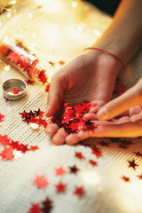 New Year and Christmas decor, a girl holding shiny red stars in a jar with a garland on a knitted white blanket