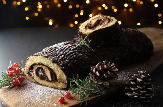 Tronchetto di Natale al cioccolato, Buche de Noel sul tagliere di legno. Decorazioni natalizie su sfondo scuro. Vista da vicino
