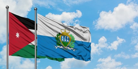 Jordan and San Marino flag waving in the wind against white cloudy blue sky together. Diplomacy...