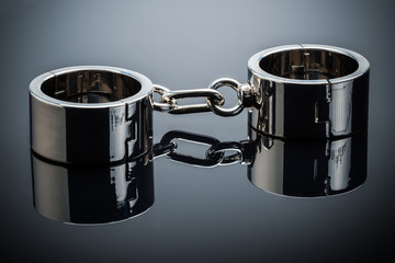 Gold handcuffs lie on a gray metal mirror surface opened for one hand. Concept tempting offer and...