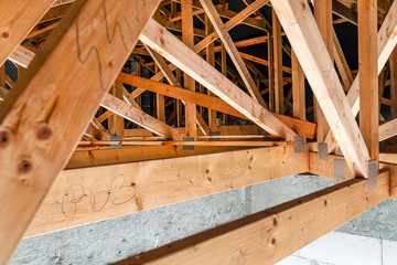 Roof trusses covered with a membrane on a detached house under construction, view from the inside, visible roof elements and truss plates.