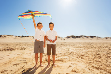 Two twin boys stand with kite on the sea beach