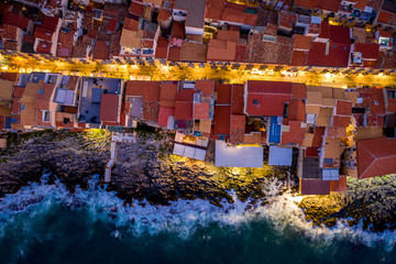 Aerial view of the rocky coast and the houses of Cefalu from the sea in windy and stormy weather. Big waves beat against stones. Streets with the city lights. Italy, Tyrrhenian SeaSicily, Italy