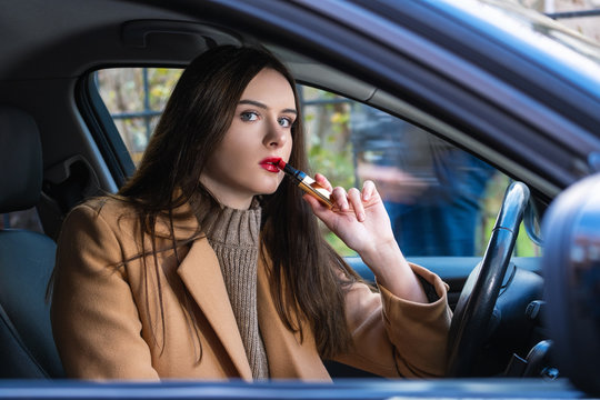 young woman driving a car with lipstick in her hands. a young woman sitting in a car behind the wheel.she's going to go.
