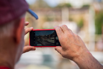 one old man travels, photographs attractions on a smartphone, close-up of hands and smartphone, rear view, summer day