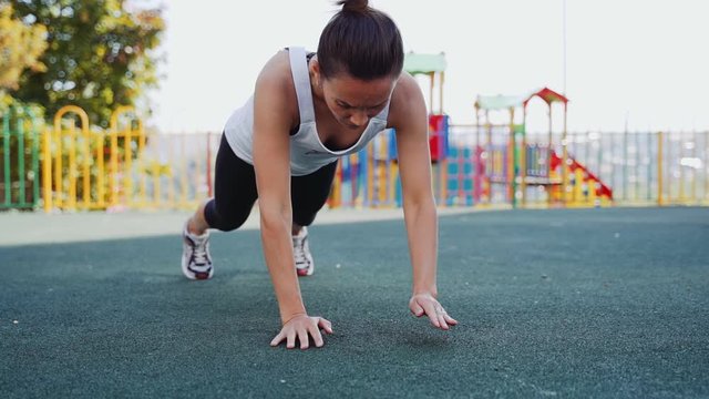 Athletic woman performs an exercise plank. The girl goes in for sports on the street.