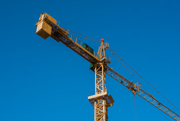 Tower crane against blue sky on a construction site for building of multi storage building or another type of structure.