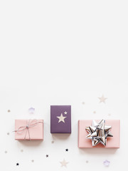 Banner with holiday presents. Gifts wrapped in pale pink and violet paper with silver ribbons and bow. Stars confetti and white copy space. Top view, flat lay.