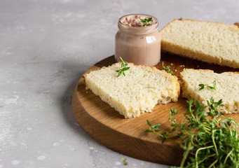 Fresh homemade chicken liver pate on bread with thyme on a wooden cutting board. 