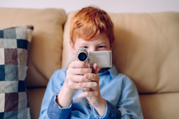 Cheerful little kid recording with a video camera at home. Isolated boy playing with technology...