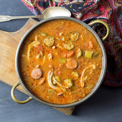 Overhead view of a bowl of gumbo shown on wood cutting board. 