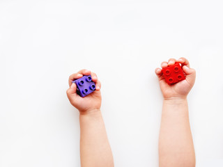 Child is holidng red and violet constructor blocks in fist. Kid's hands with bricks toy on white background. Educational toy, flat lay, top view.