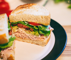 Turkey club sandwich with bacon, avocado and tomato on sourdough bread, cut into two halves. 