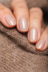 Nude color manicure on short round natural nails with brown knitted scarf - obrazy, fototapety, plakaty
