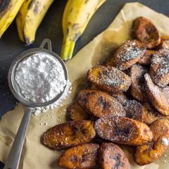 Freshly made fried sweet plantains called maduros, shown with powdered sugar on brown kraft paper. 