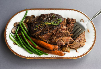 Slow cooked beef roast with carrots and green beans with thyme garnish. 