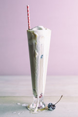 Tall root beer float in a pilsner glass with red paper straw, melting ice cream and cherry. 