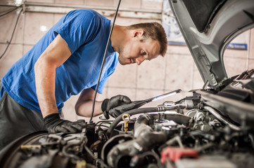 Naklejka na ściany i meble Car mechanic repairer service technician checks and repairs auto engine
