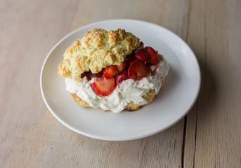 One strawberry shortcake on a white plate with fresh whipped cream. 