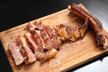 Medium-roasted steak cut into pieces on a wooden board with sauce and seasonings. Delicious steak. Beef steak medium rare on vegetable cushion. Beef steak on wooden plate. 