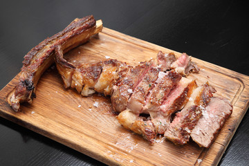 Medium-roasted steak cut into pieces on a wooden board with sauce and seasonings. Delicious steak. Beef steak medium rare on vegetable cushion. Beef steak on wooden plate. 