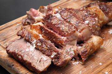 Medium-roasted steak cut into pieces on a wooden board with sauce and seasonings. Delicious steak. Beef steak medium rare on vegetable cushion. Beef steak on wooden plate. 