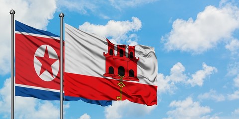 North Korea and Gibraltar flag waving in the wind against white cloudy blue sky together. Diplomacy...