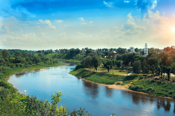 Fototapeta na wymiar red church with blue domes from Rzhev town on the shore surrounded by green trees, view from Volga river at sunny summer day