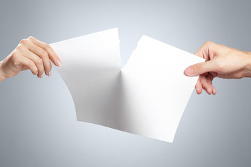 Hands tearing a sheet of white paper in half on gray background