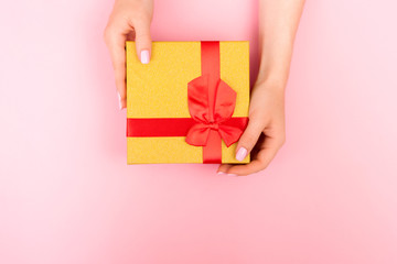 Yellow gift box on a pink background. Beautiful hands of a young girl with pink nails.