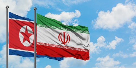 North Korea and Iran flag waving in the wind against white cloudy blue sky together. Diplomacy concept, international relations.