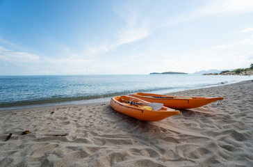 Fototapeta premium Two colorful orange kayaks on a sandy beach ready for paddlers in sunny day. Several orange recreational boats on the sand. Active tourism and water recreation.