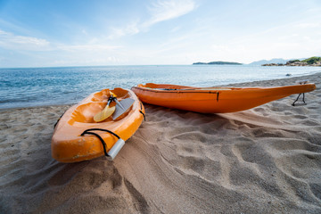 Two colorful orange kayaks on a sandy beach ready for paddlers in sunny day. Several orange...