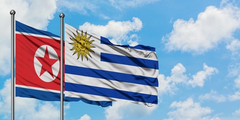 North Korea and Uruguay flag waving in the wind against white cloudy blue sky together. Diplomacy...