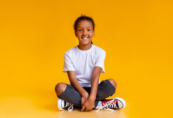 Cute black girl sitting on floor in studio and smiling