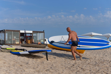 A man walks along a sandy beach and carries a sub-Board in his hand