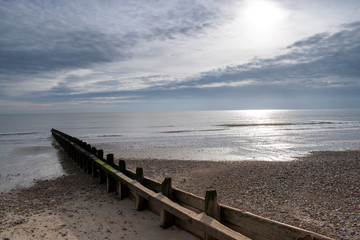 Obraz premium Littlehampton, England, beach at low tide showing a silky smooth sea and dramatic clouds with the sun reflecting of the water behind the clouds on a beautiful Autumn morning.