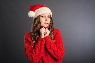 Cute and beautiful girl in red sweater and Santa hat on grey background. The concept of new year and Christmas, shopping. Place for your advertisement or text template