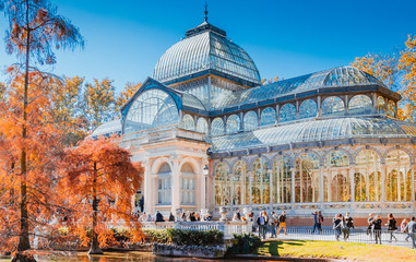 Crystal Palace in Retiro Park in Madrid autumn colorful view with people, trees, plants and environment - obrazy, fototapety, plakaty