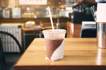 Ice coffee in plastic cup on brown wooden table at cafe