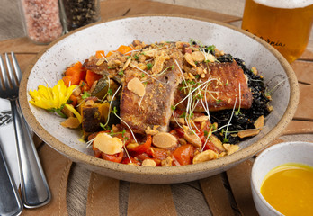 Grilled fish, black rice and vegetables on a bowl with salt, pepper, sauce and soda