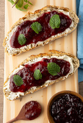 Plain bread, cream cheese, berries jam and mint leaves over wooden board