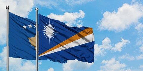 Kosovo and Marshall Islands flag waving in the wind against white cloudy blue sky together....