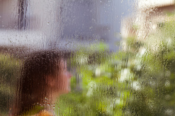 Wet window glass with blurred silhouette of woman head